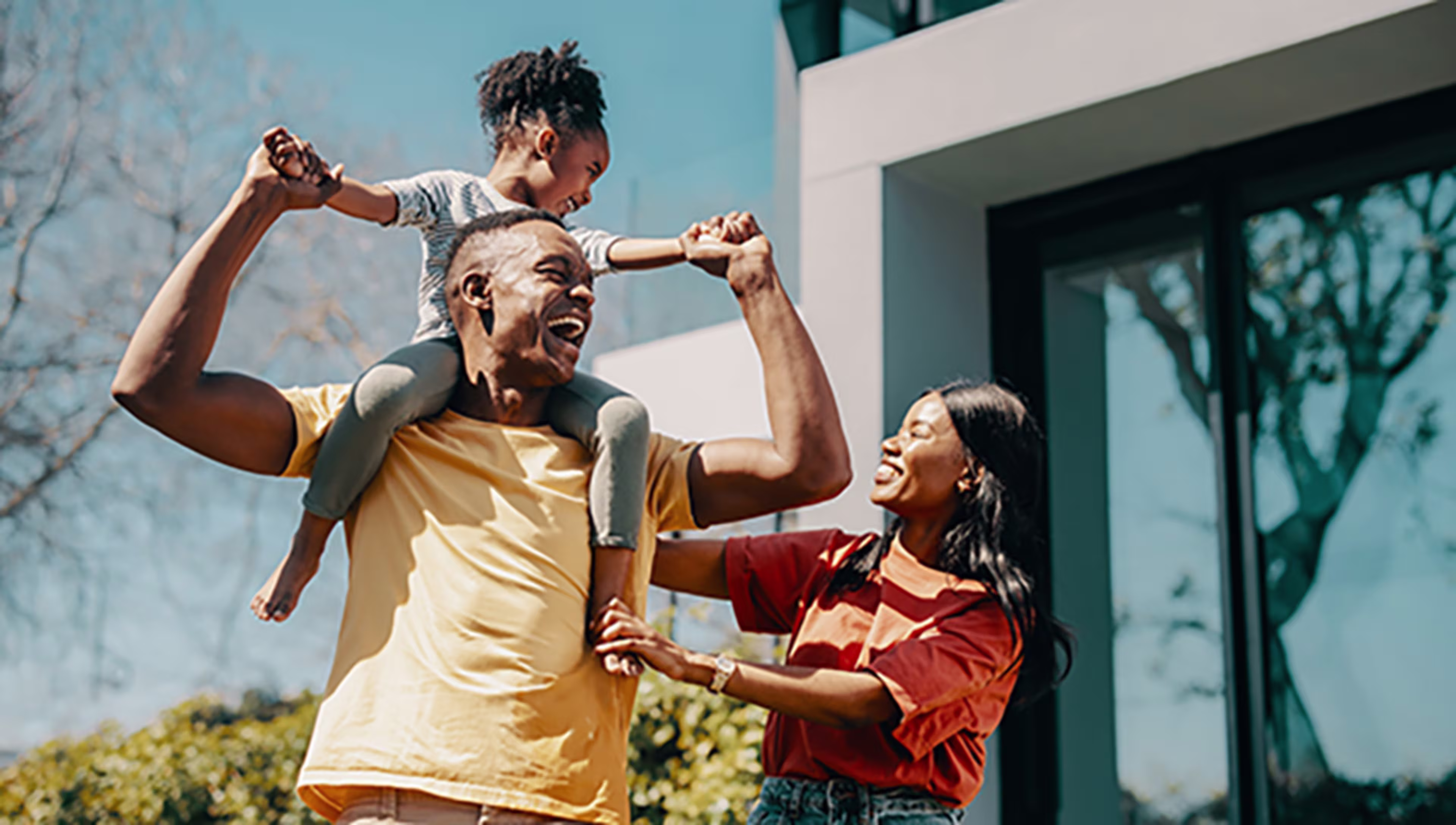 Mom and Dad with child on shoulders in front of a house