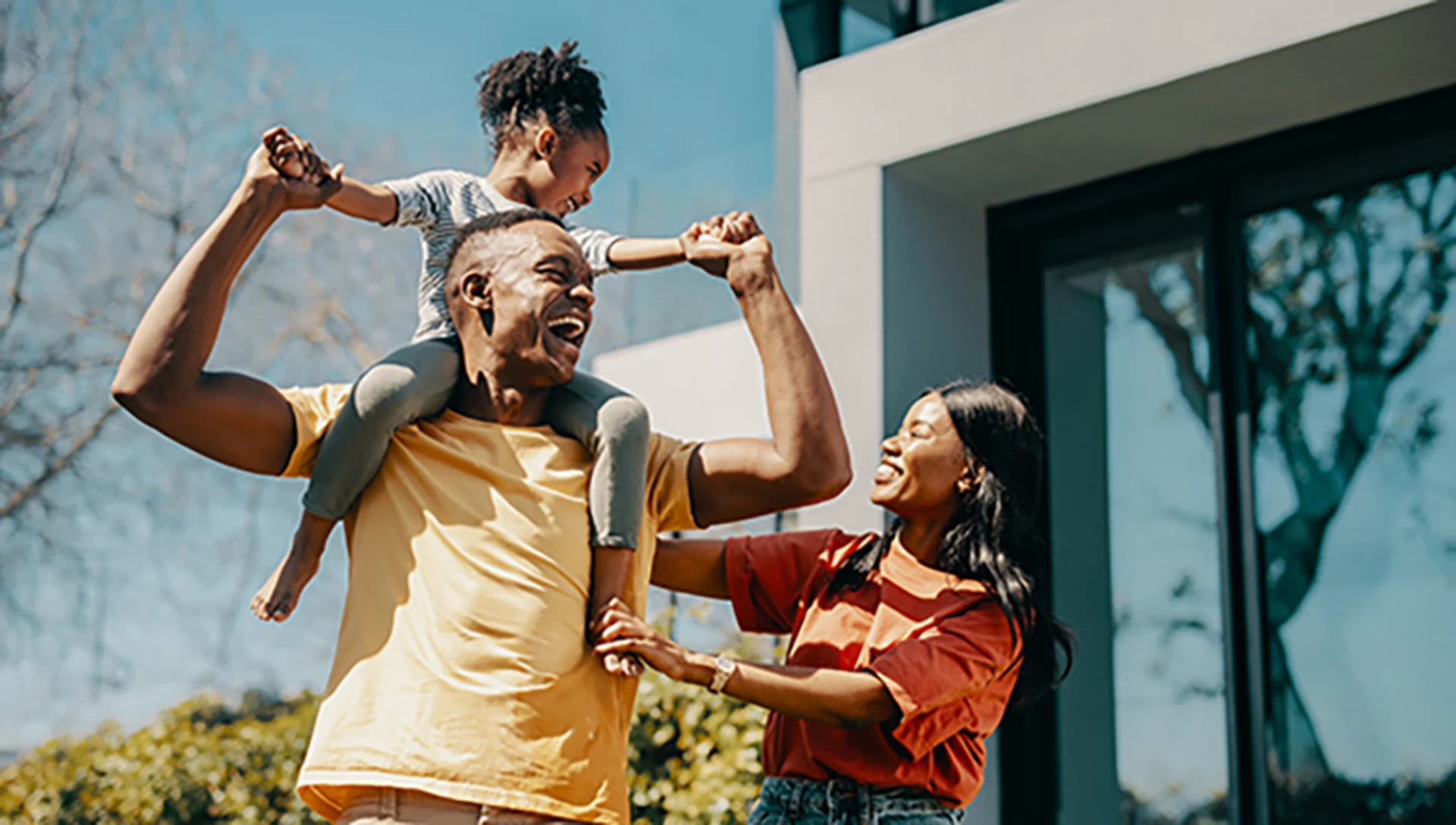 Mom and Dad with child on shoulders in front of a house