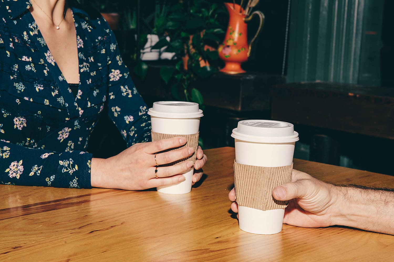 Two friends holding cups of coffee across a table