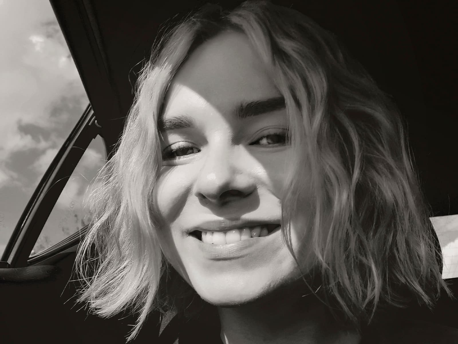 Black and white close-up of a girl's smiling face in a car