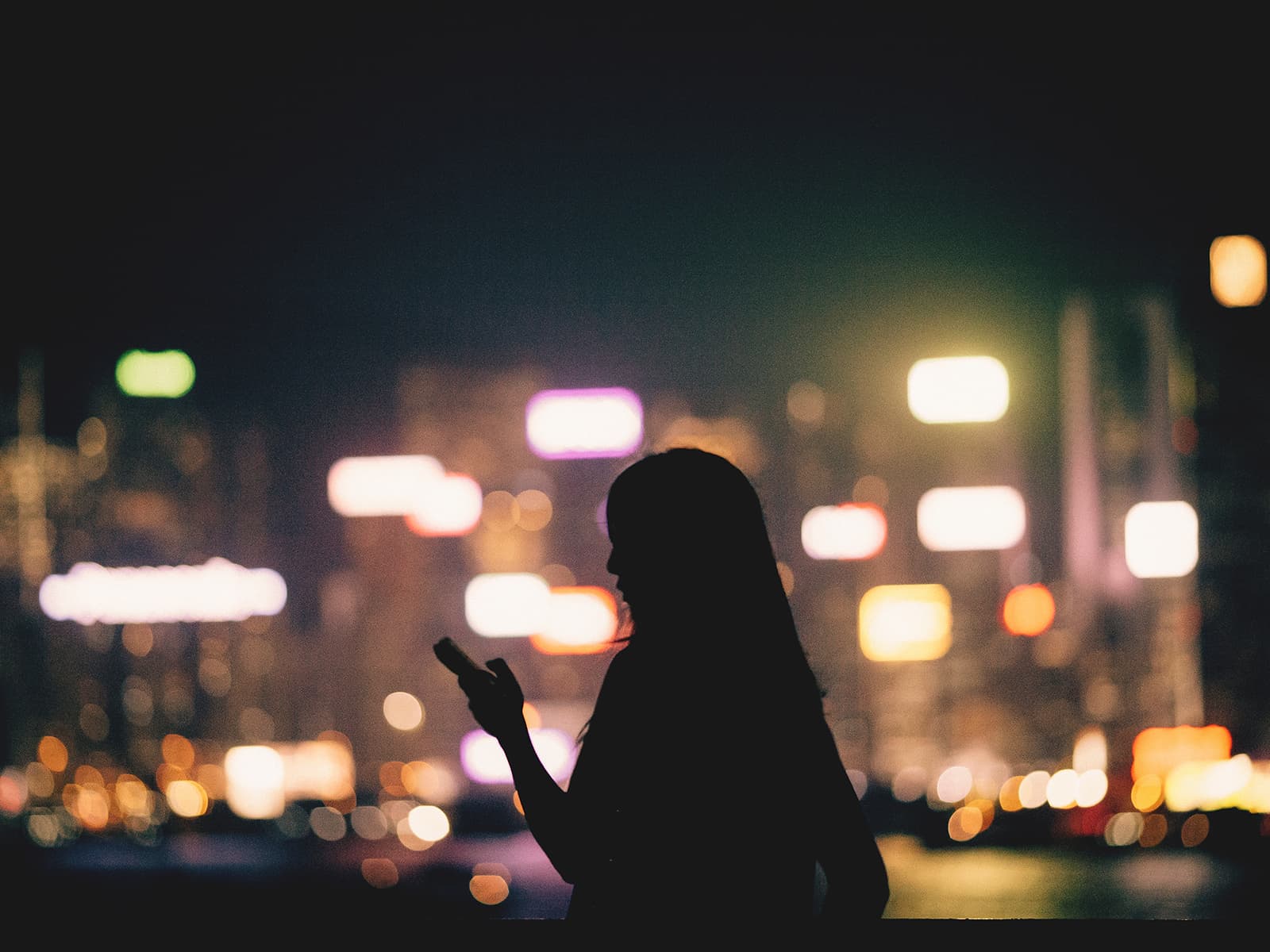 Silhouette of woman holding her phone against the nighttime city skyline