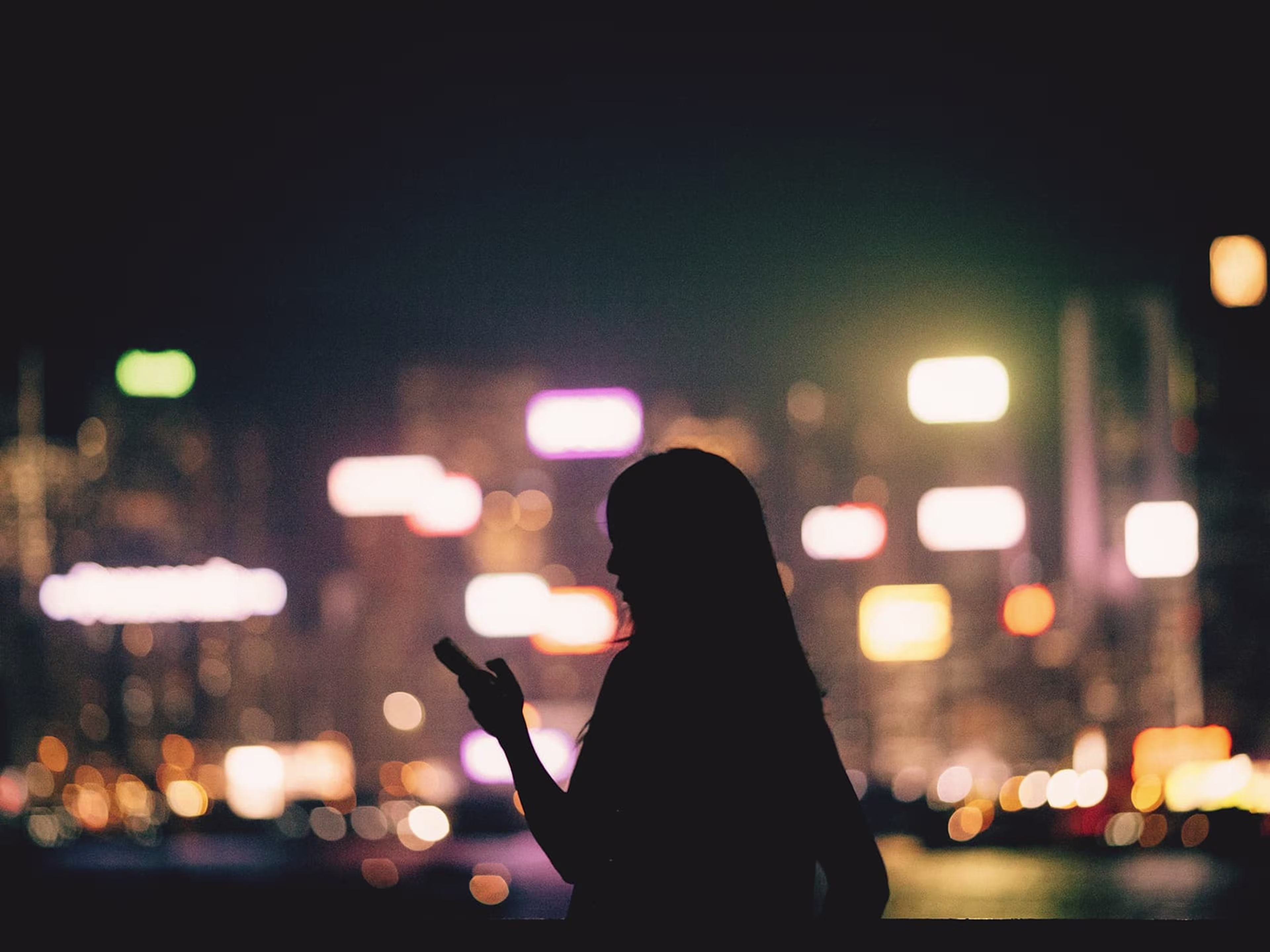 Silhouette of woman holding her phone against the nighttime city skyline
