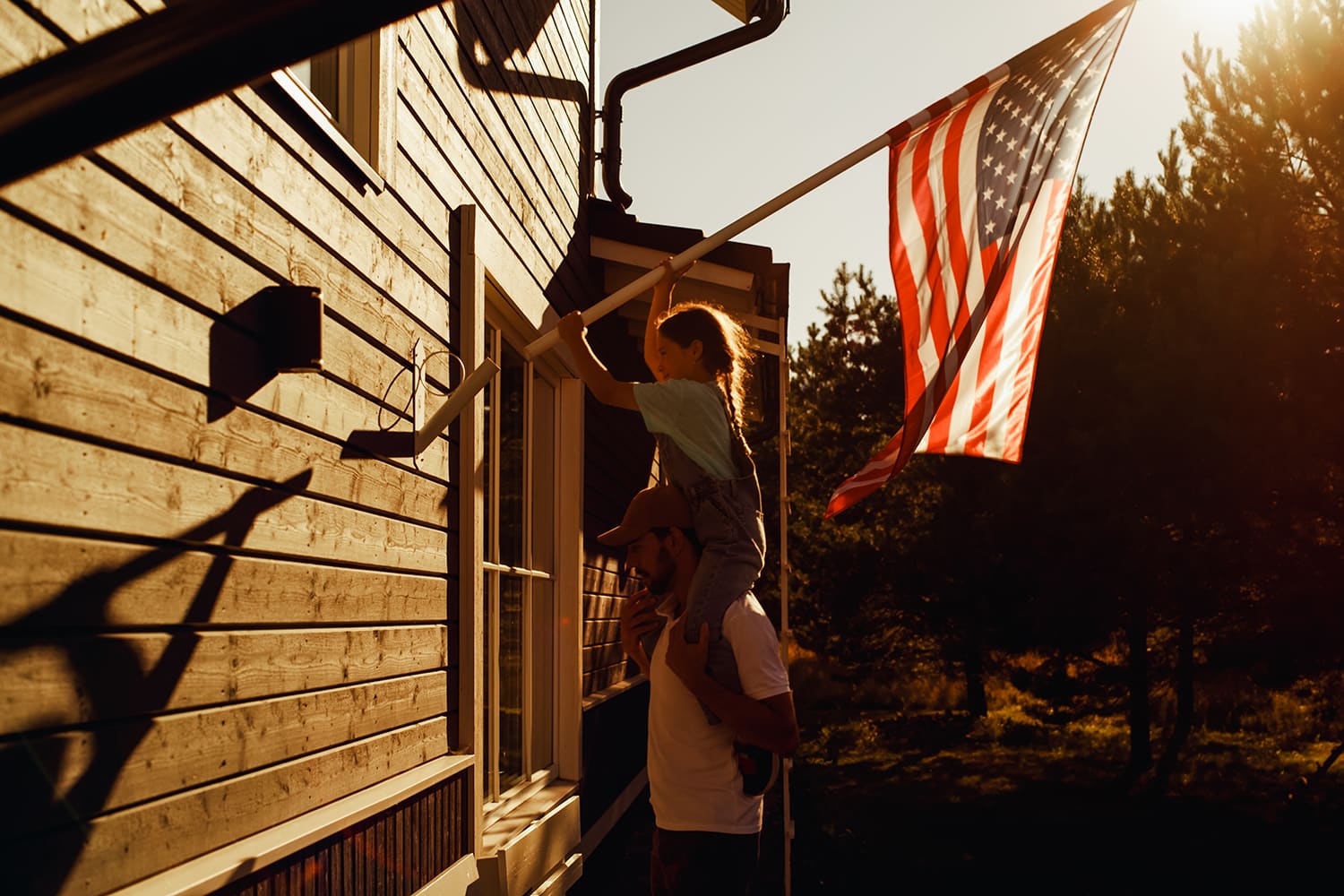 Photo of a girl on her dad's shoulders, setting up an American flag.