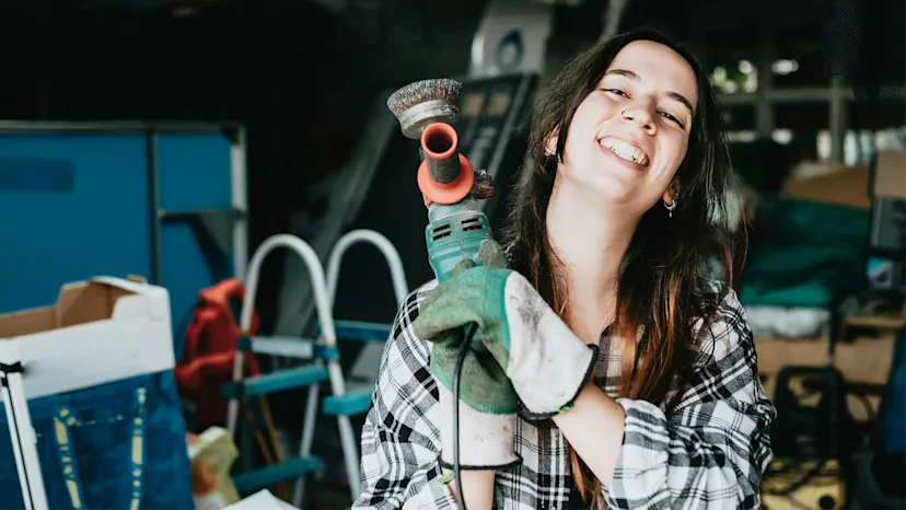Smiling woman holding a power tool, representing a confident small business owner in a skilled trade or construction business