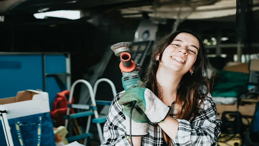 Smiling woman holding a power tool, representing a confident small business owner in a skilled trade or construction business