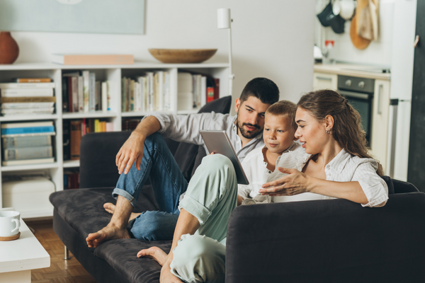 Two adults and a child sitting on a couch looking at a tablet together.