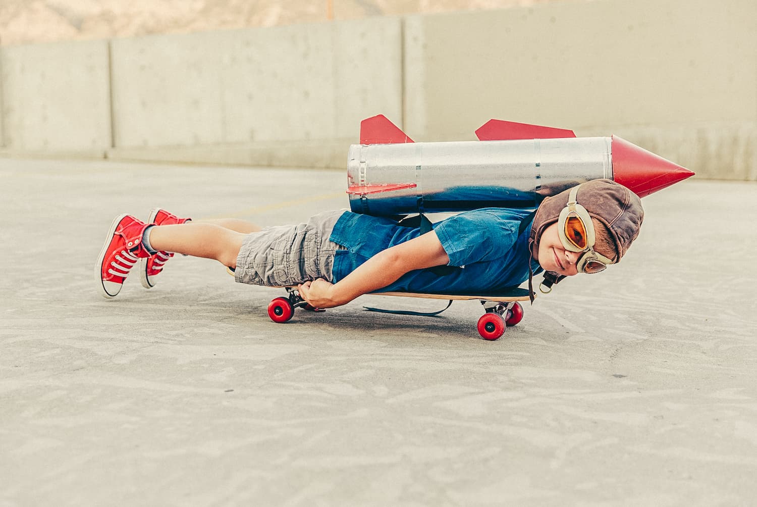 Boy rides a skateboard while wearing a toy rocket pack on his back.