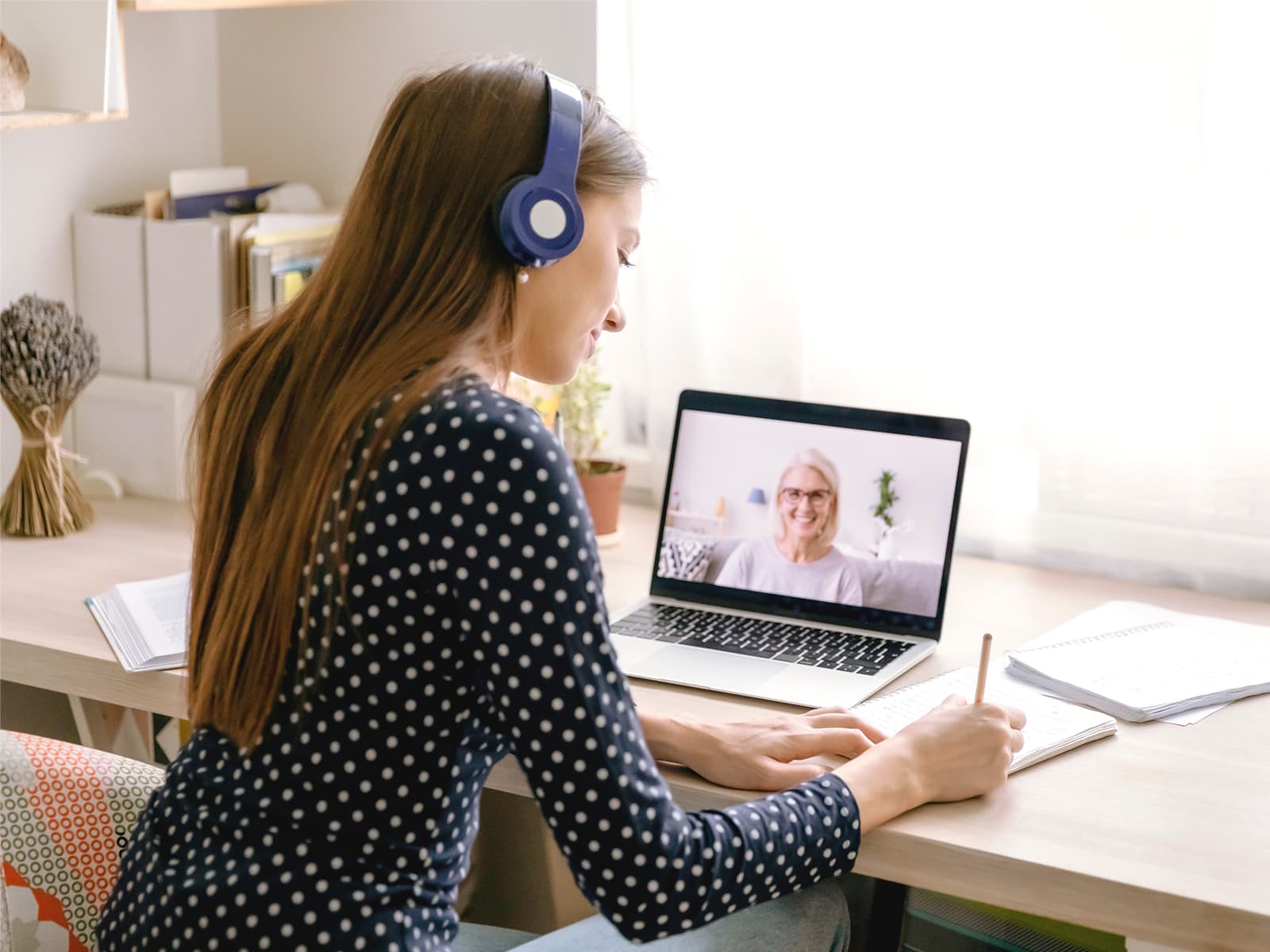 Girl with headphones on and taking notes while on a video conference with a financial expert