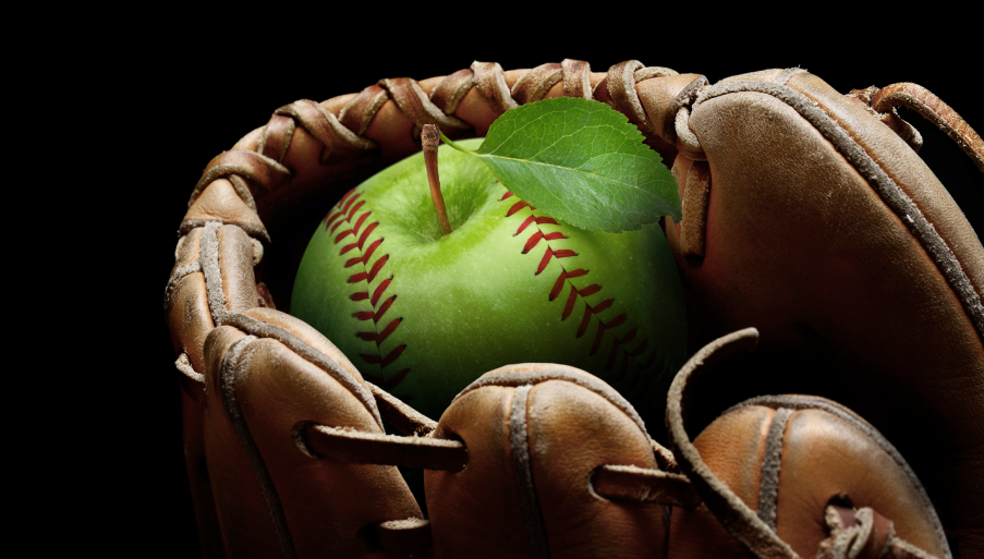 Baseball mitt holding an apple. The apple has baseball stitches on it.