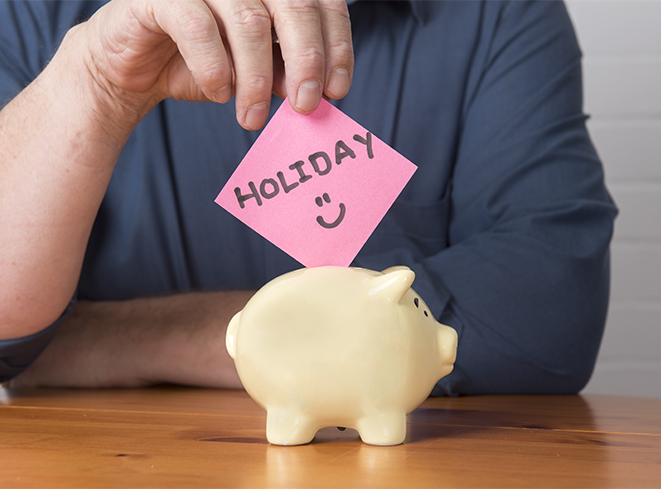 Man putting sticky note into piggy bank that says "Holiday :)"