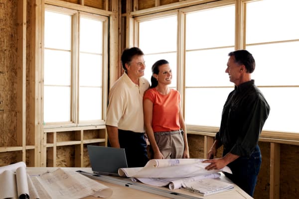 An adult couple speaking to a contractor in a room that is under construction