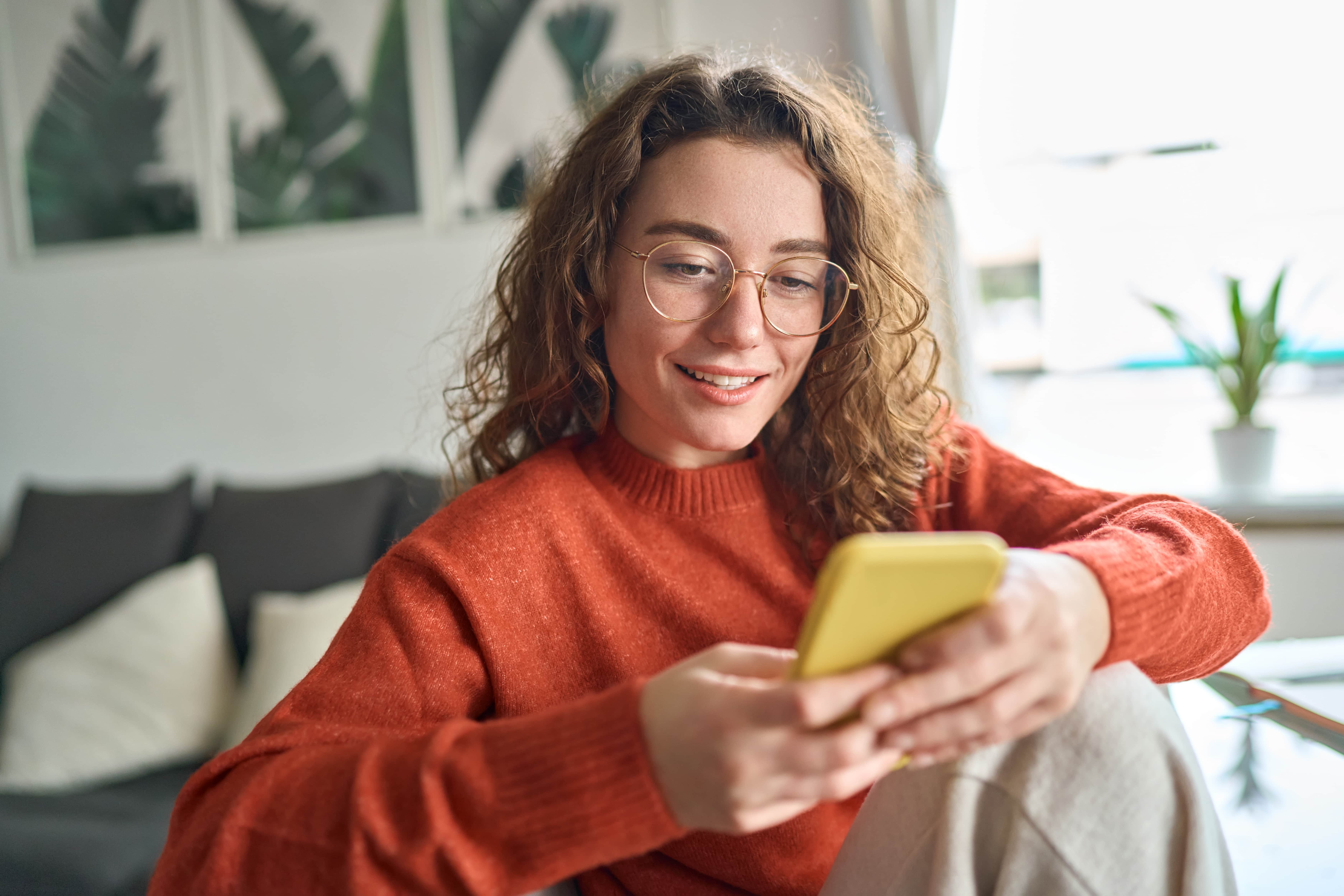 Young woman with glasses looking at her phone and smiling