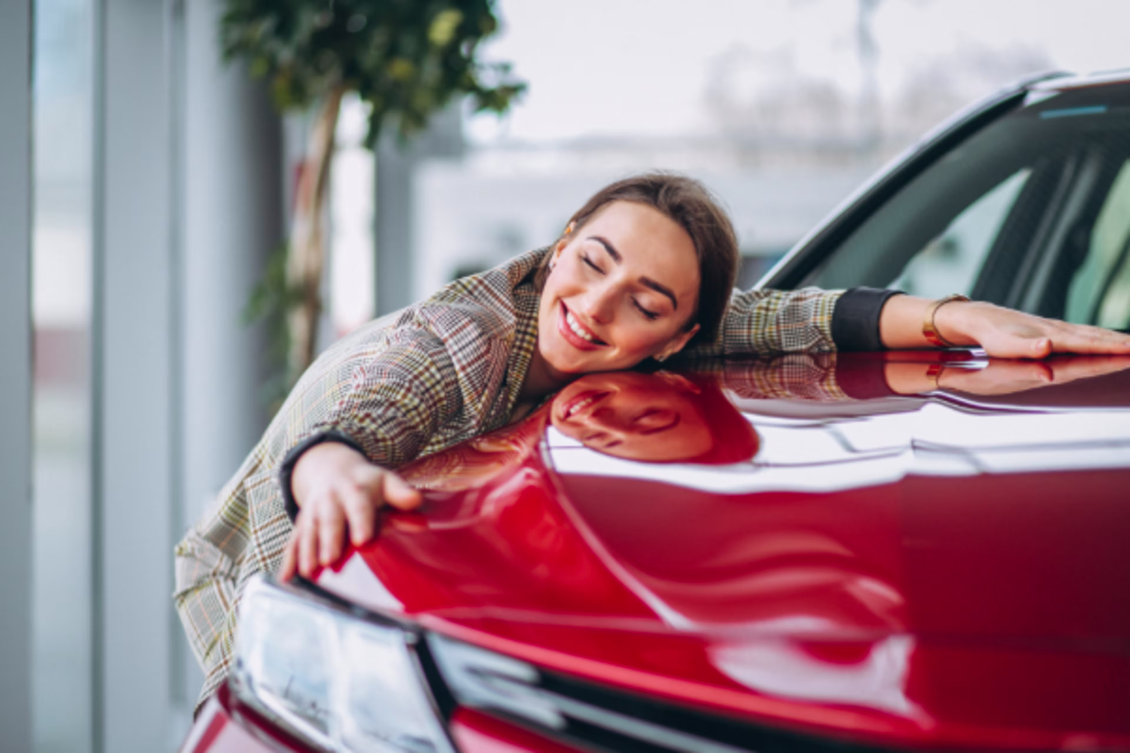Photo of a young woman hugging the hood of a red car