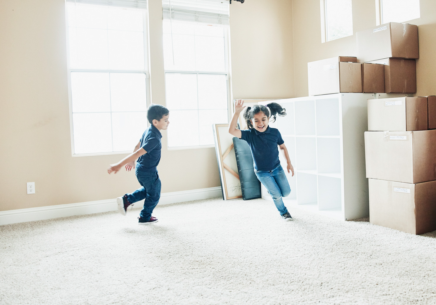 Two young boys chasing each other in a room with moving boxes