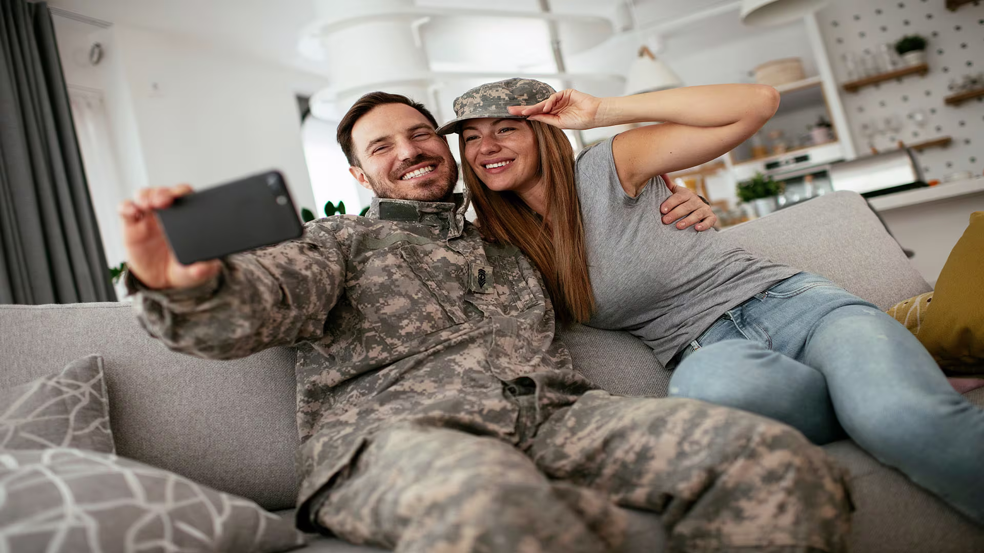 Man in service uniform and woman taking a selfie on the couch, celebrating moments of homeownership with the support of VA Mortgage Loans, VA Home Loans, and home improvement opportunities through a VA Loan.