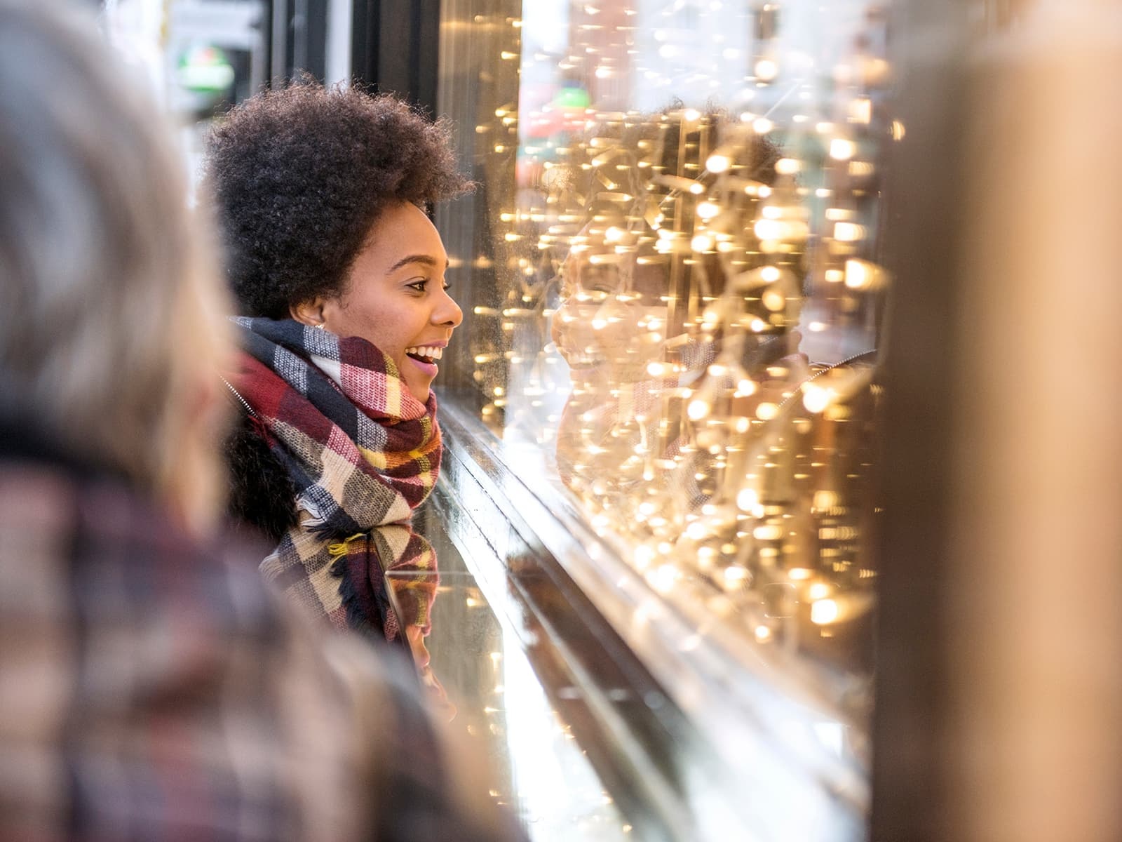 Woman wearing a scarf looking into a holiday window display with lights
