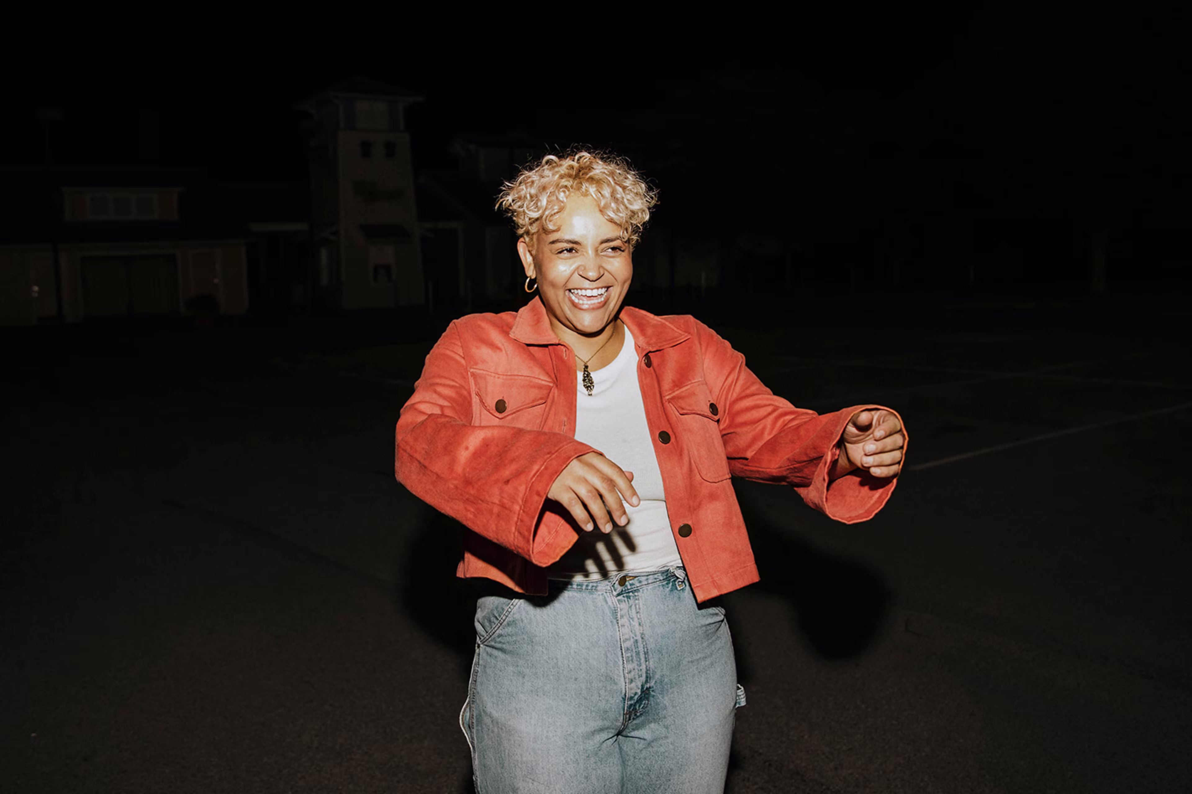 Person dancing in orange jacket, dark background