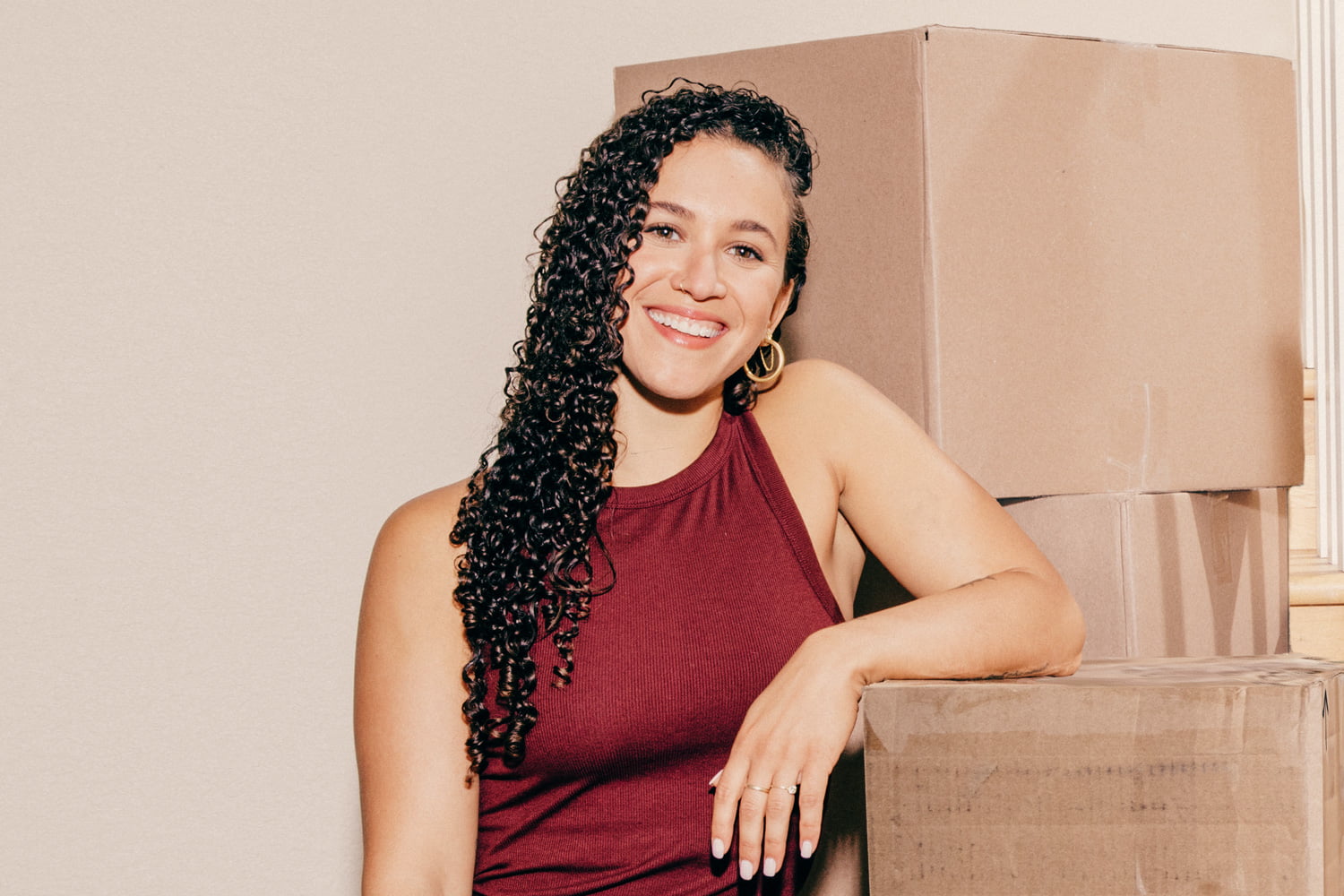 A smiling young lady is in front of moving packing boxes in her new home,