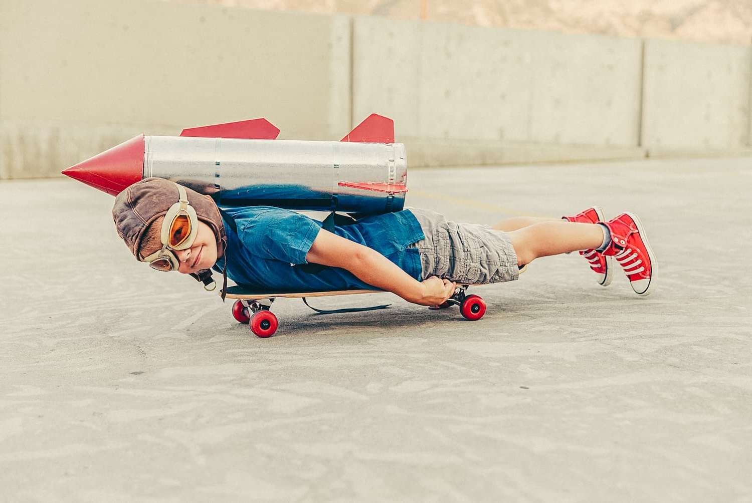 Boy rides a skateboard while wearing a toy rocket pack on his back.