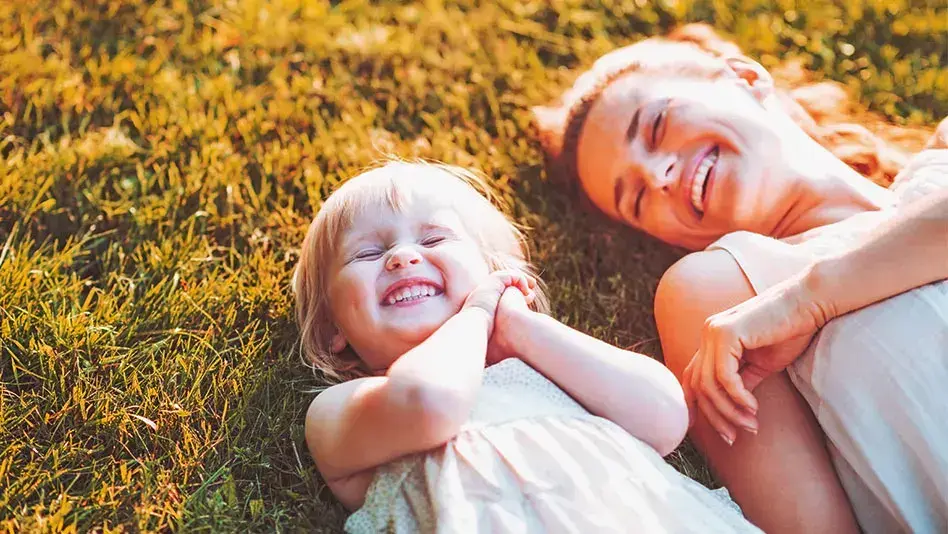 A young girl and a woman laughing in the grass.