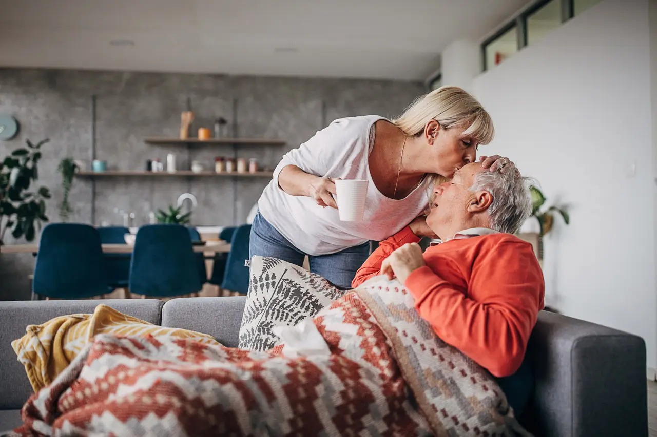 Older women handing a cup of tea to a sick older man on the couch