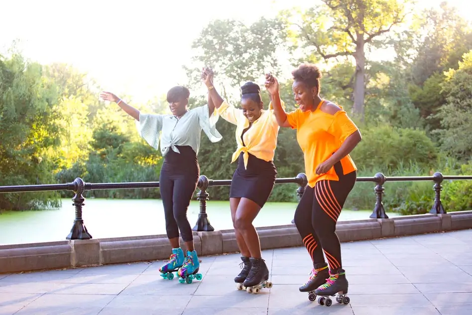 Three happy women holding hands and roller skating at the park