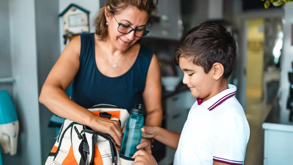 Woman helping a little boy pack a water bottle into his backpack