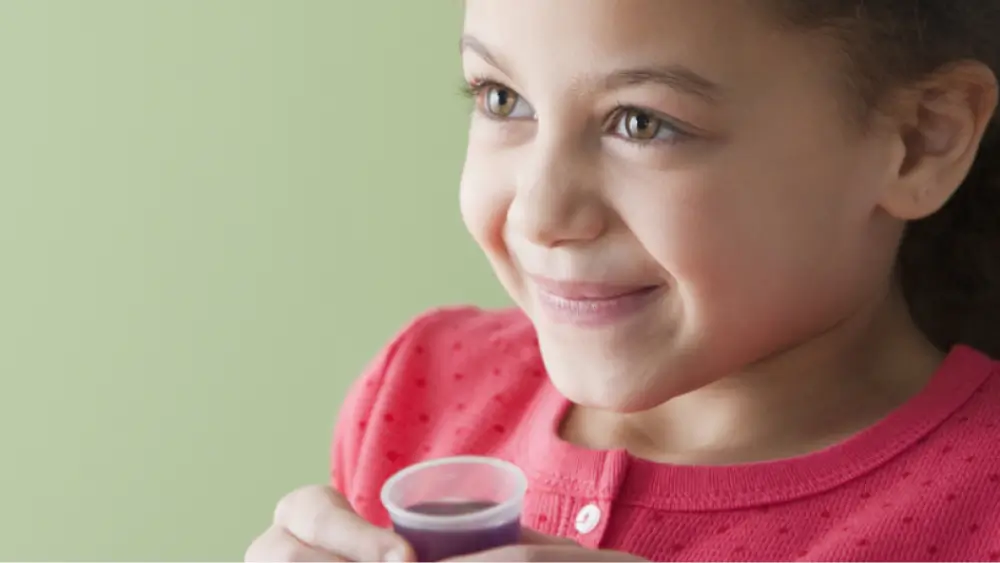 Little girl holding dosing cup of purple liquid medicine