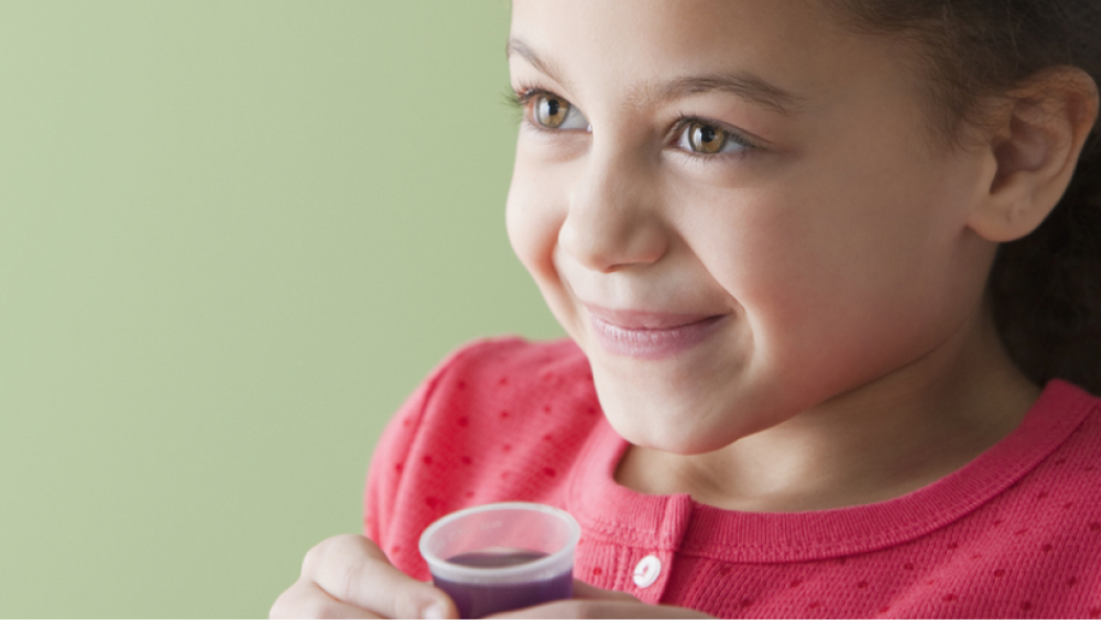 Little girl holding a dosing cup full of purple liquid medicine