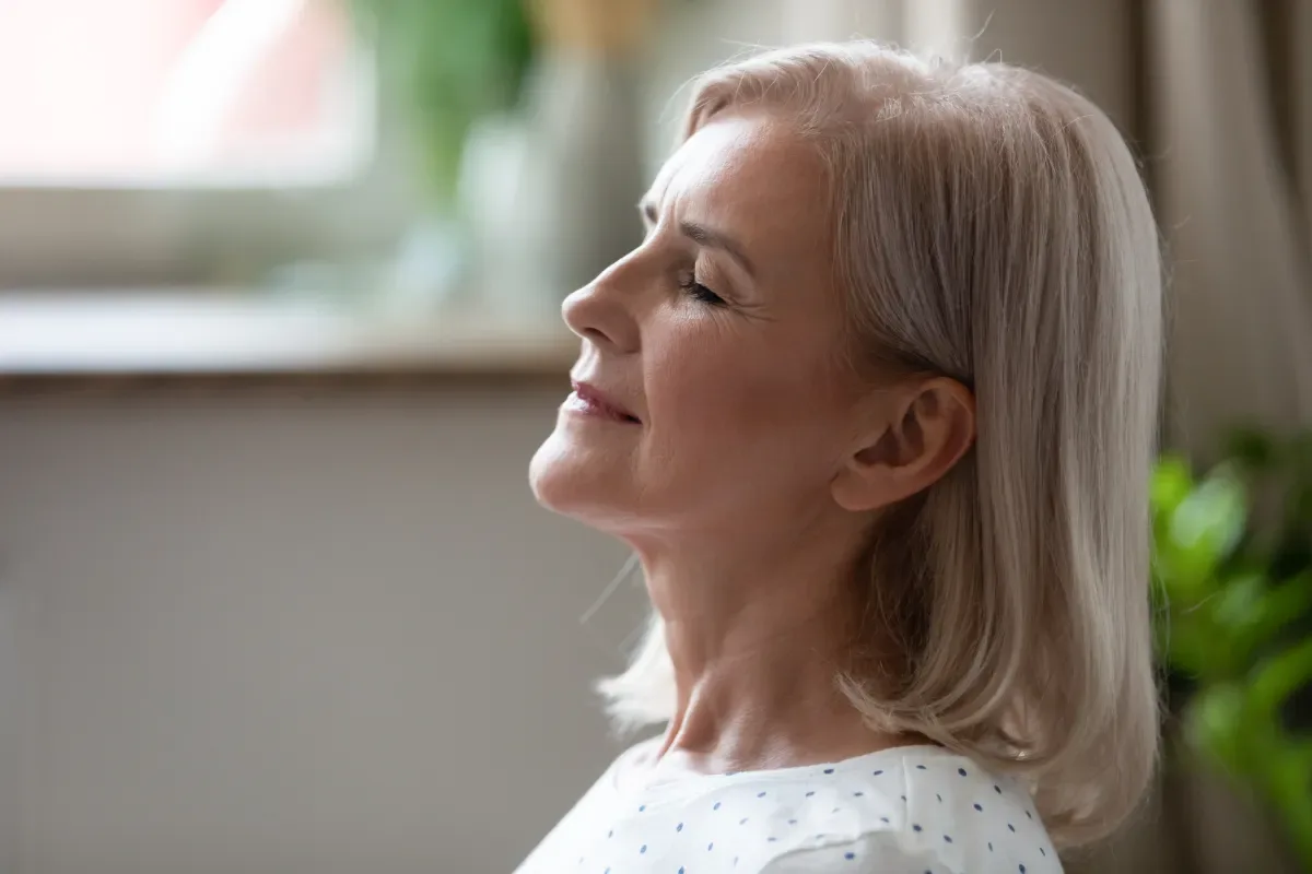 Meditatie en spierontspanning - vrouw met ogen dicht in woonkamer