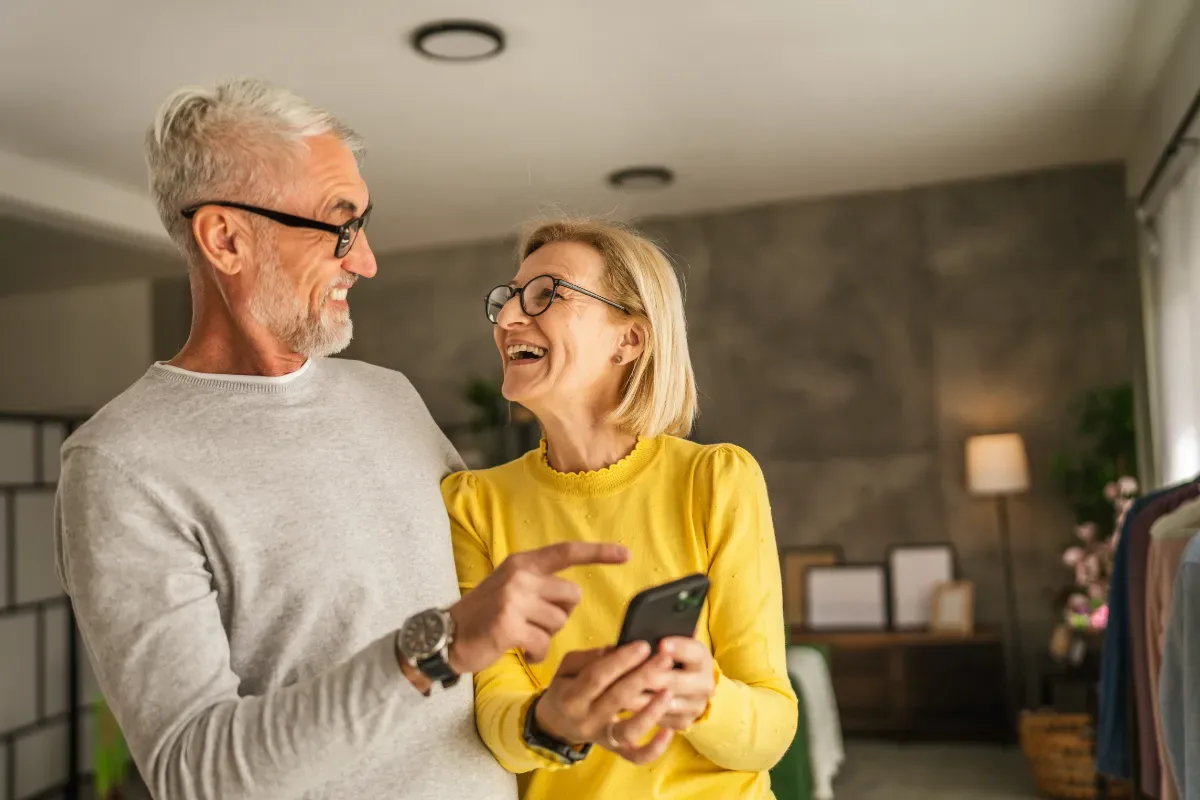 Positieve emotie - man en vrouw lachen uitbundig met telefoon in hand in woonkamer