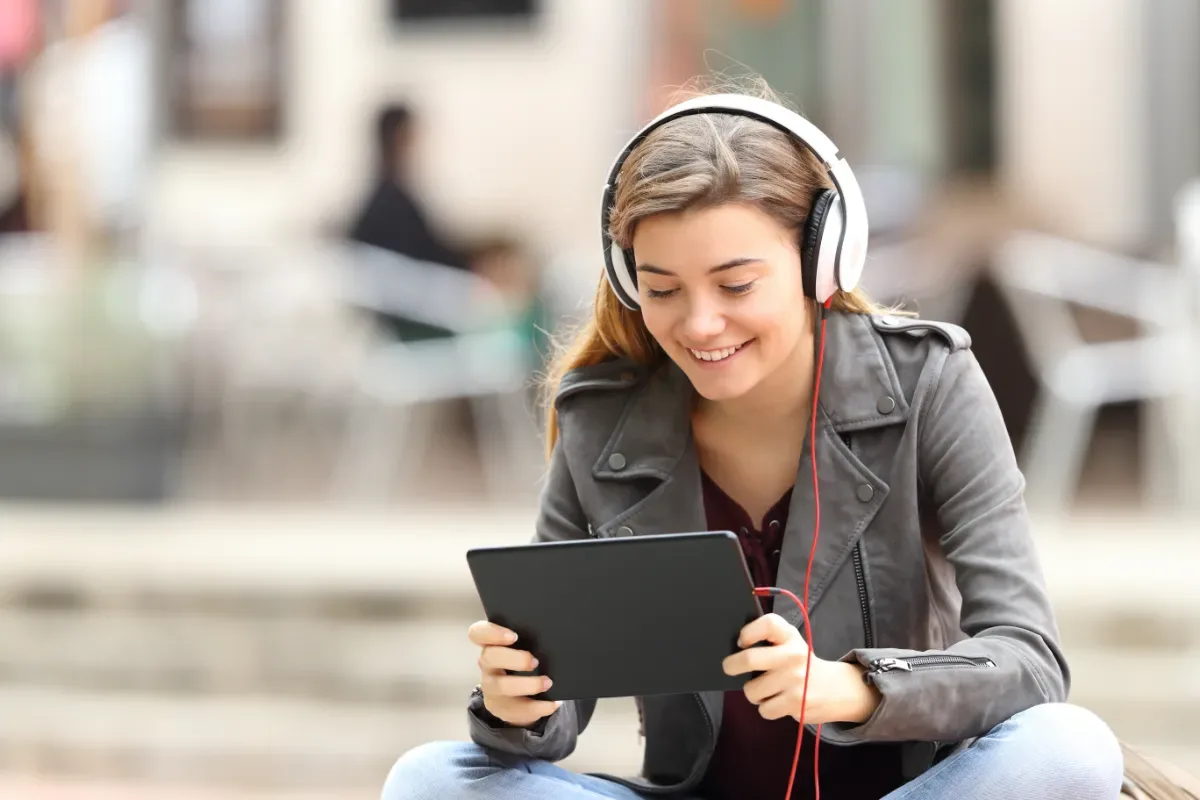 Positieve emotie - vrouw zit buiten met koptelefoon achter tablet