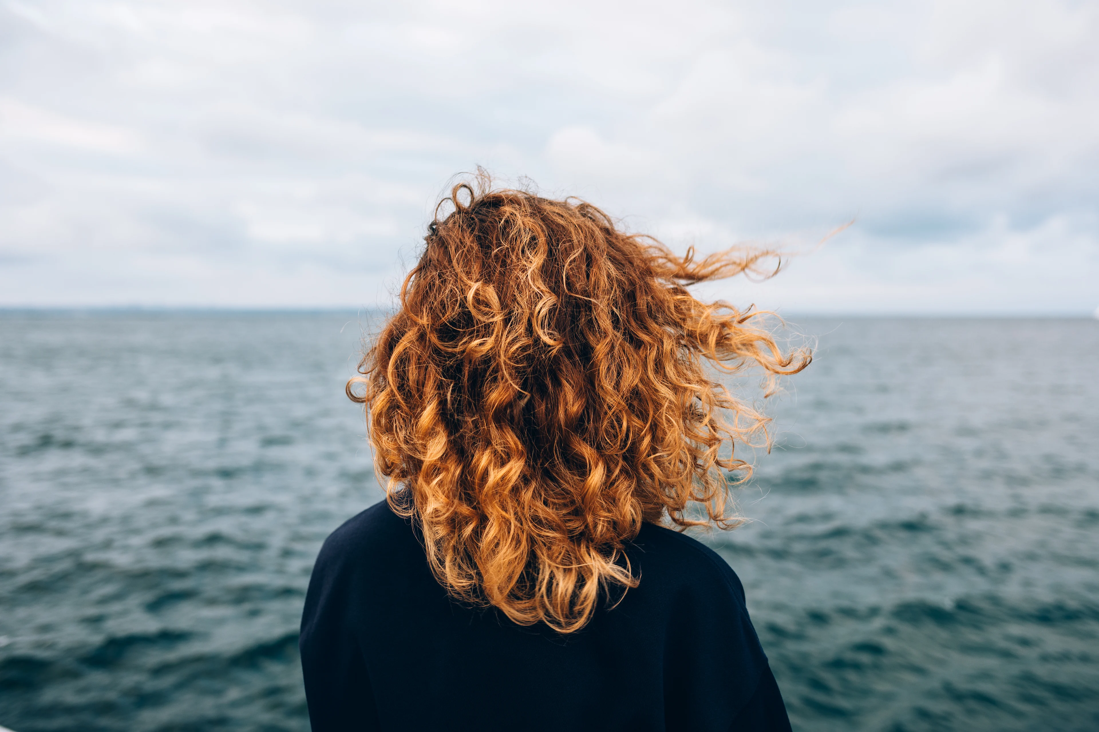 Stress verminderen met ontspanningsoefeningen - vrouw met rode krullen kijkt naar de zee