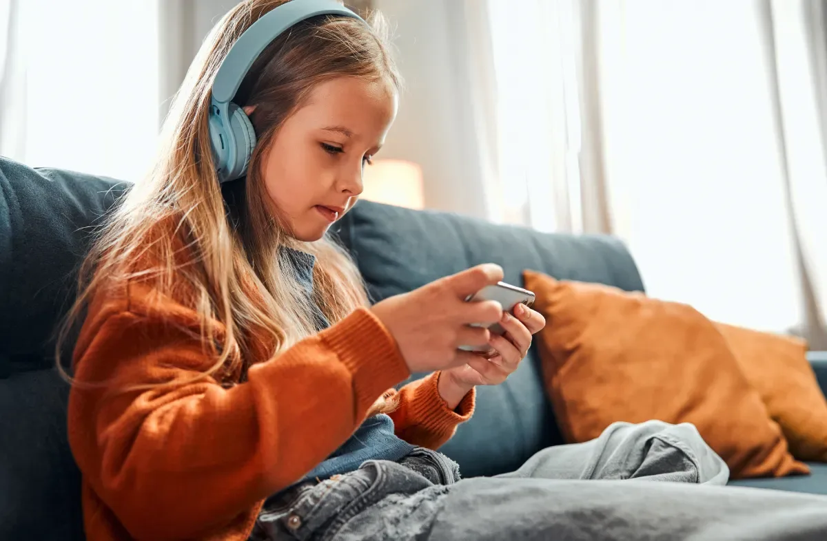 Nederlandse kinderen te vroeg naar bed - kind op bank met koptelefoon en telefoon