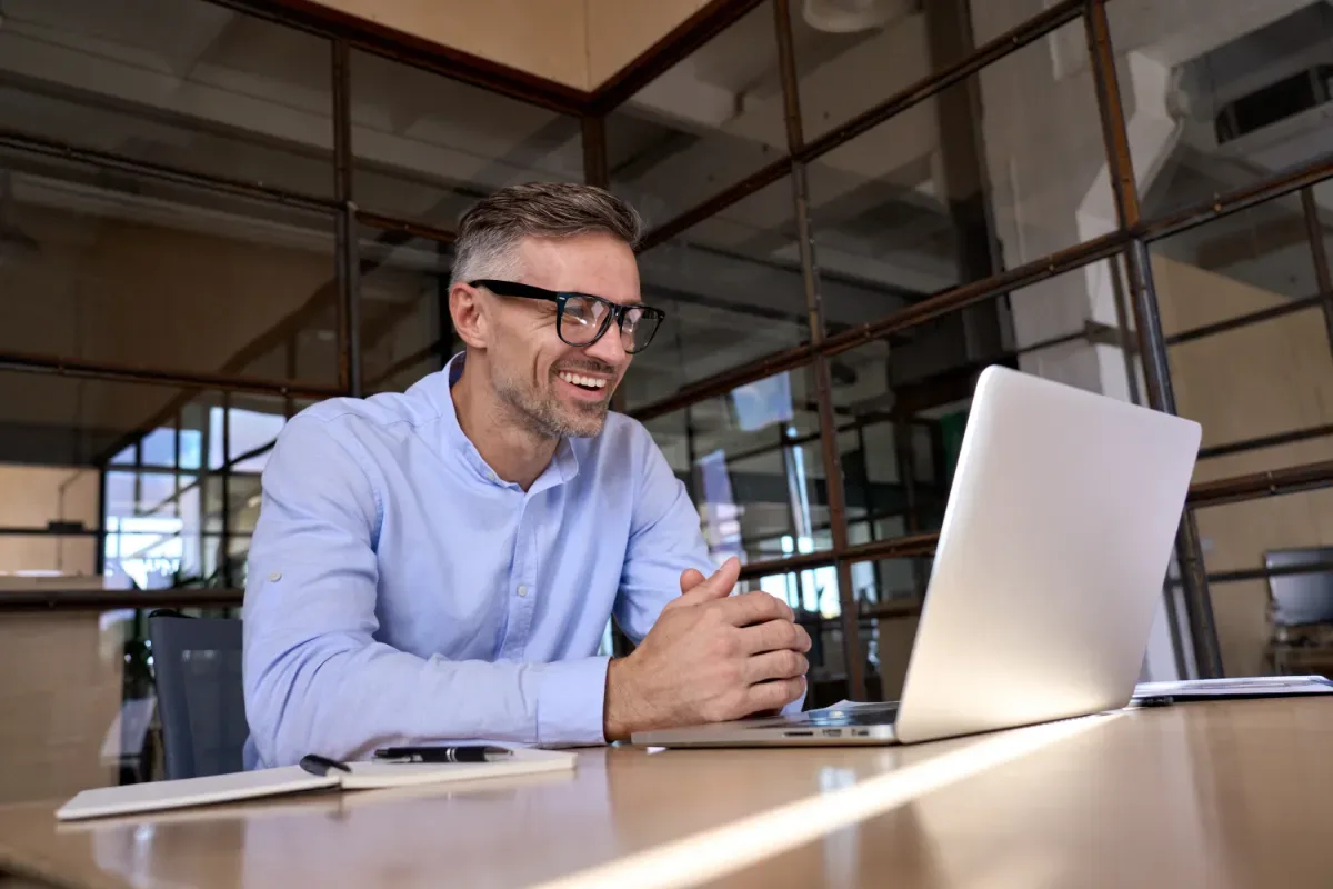 Scholing en training - man op kantoor lacht breed achter laptop