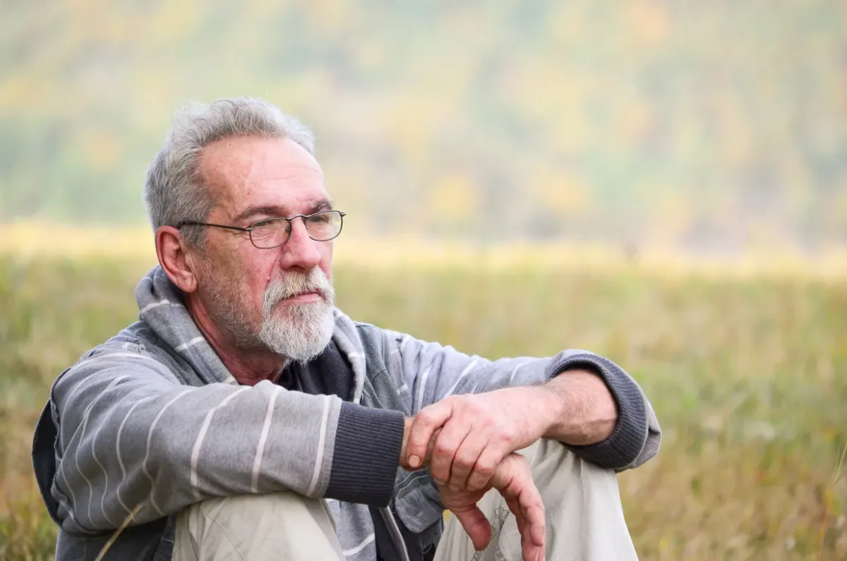 Stress verminderen door geldzorgen te delen - zittende man staart voor zich uit in natuur