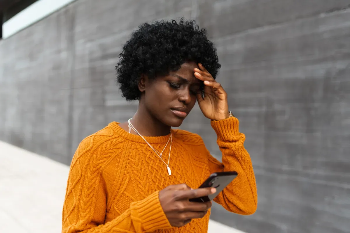 Burn-out kenmerken: hoe weet je het zeker? - vrouw kijkt moeilijk naar telefoon en grijpt naar hoofd