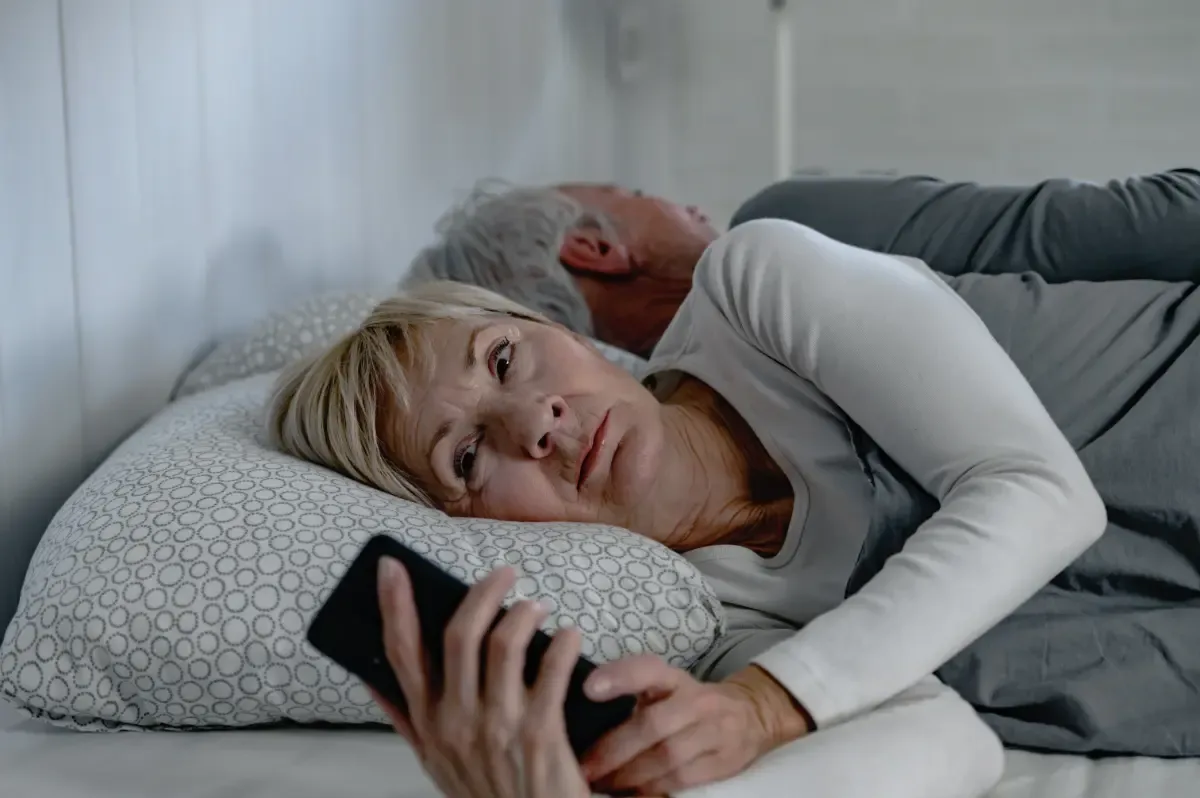 Wat veroorzaakt insomnia? - vrouw ligt rusteloos naast man in bed op telefoon