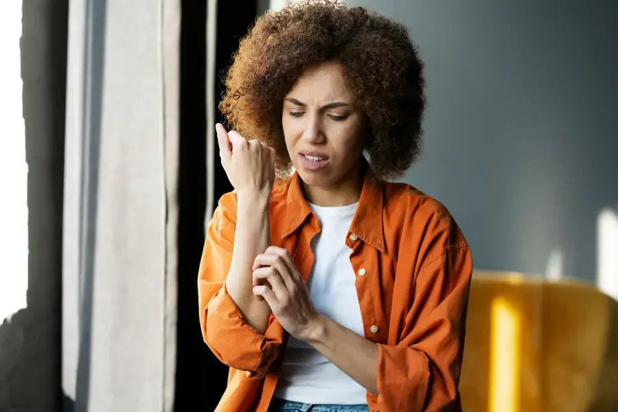 Stress, jeuk en bultjes: hoe zit dat precies? - Symptomen en oplossingen - vrouw krabt aan arm kijkt gefrustreerd 2