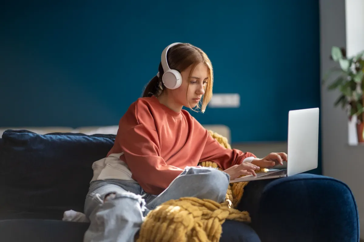 Ontspannen - jonge vrouw zit met koptelefoon en laptop op de bank