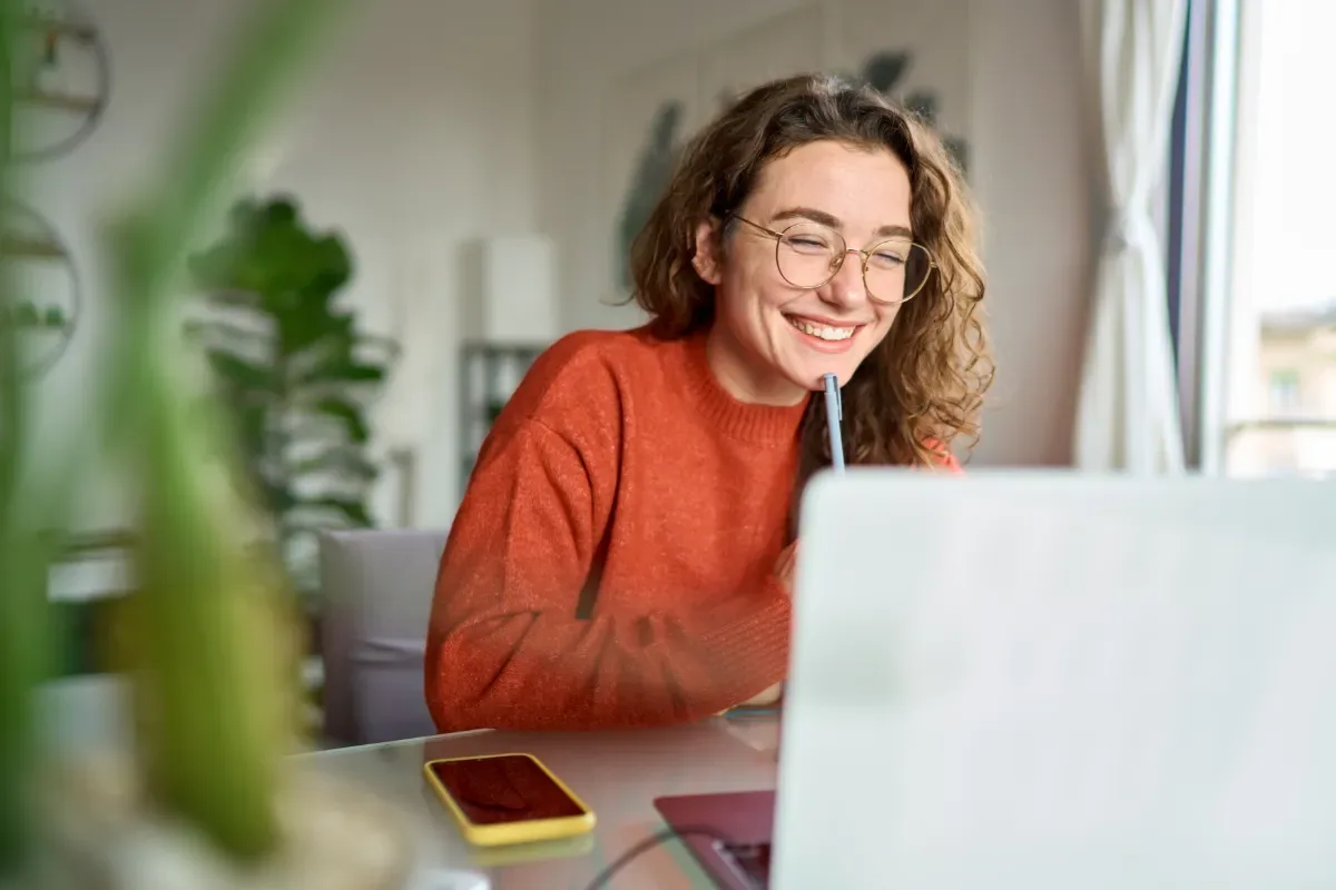 Positieve emotie - vrouw lacht breed naar laptop met pen bij gezicht