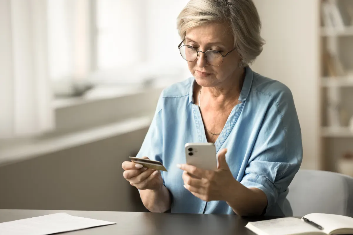 Hulp met schulden: je staat er niet alleen voor - vrouw kijkt naar telefoon en pasje