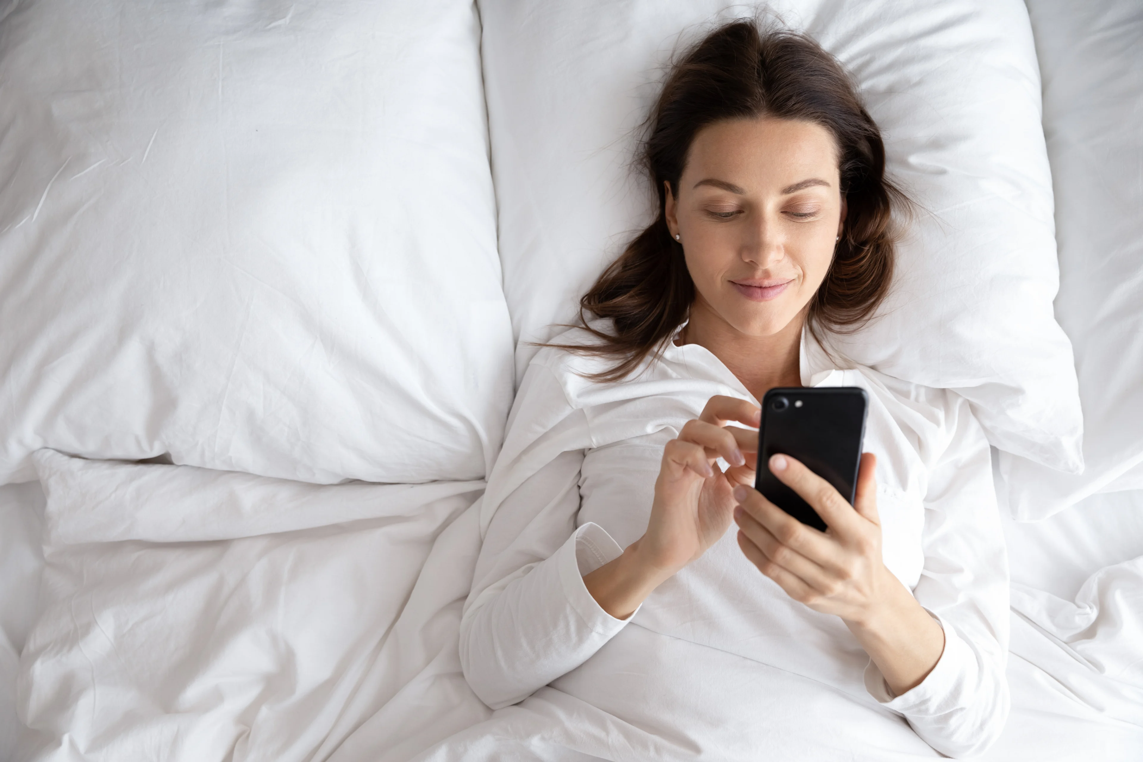 Alternatieven voor slaapmedicatie - Vrouw ligt in bed op telefoon te scrollen