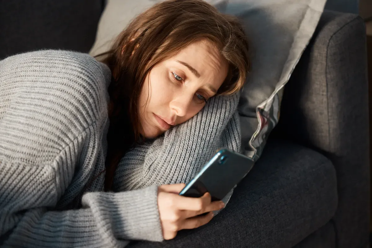 Verslaving - vrouw ligt bedroefd en kijkt naar telefoon