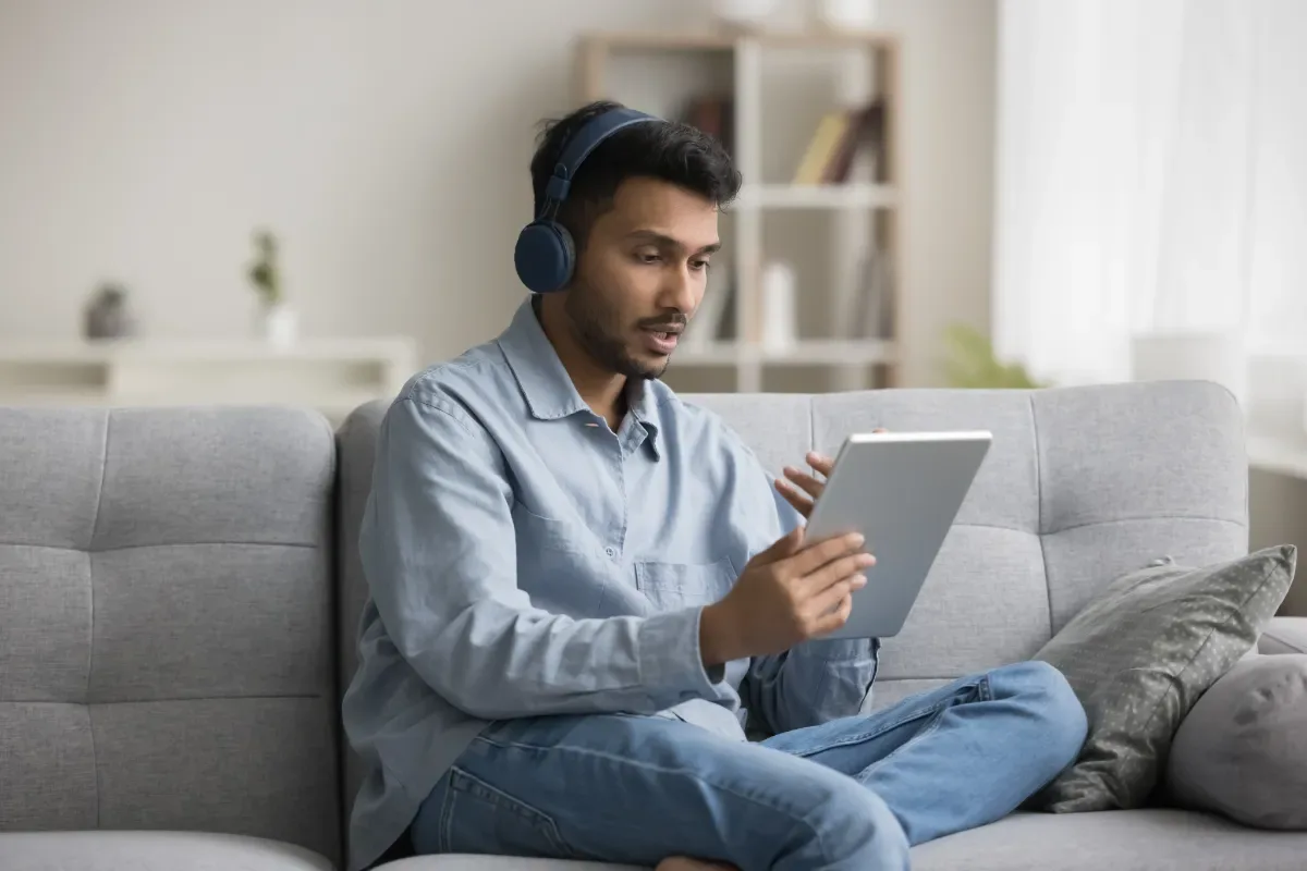 Consultatie - jonge man zit pratend met tablet en koptelefoon op de bank