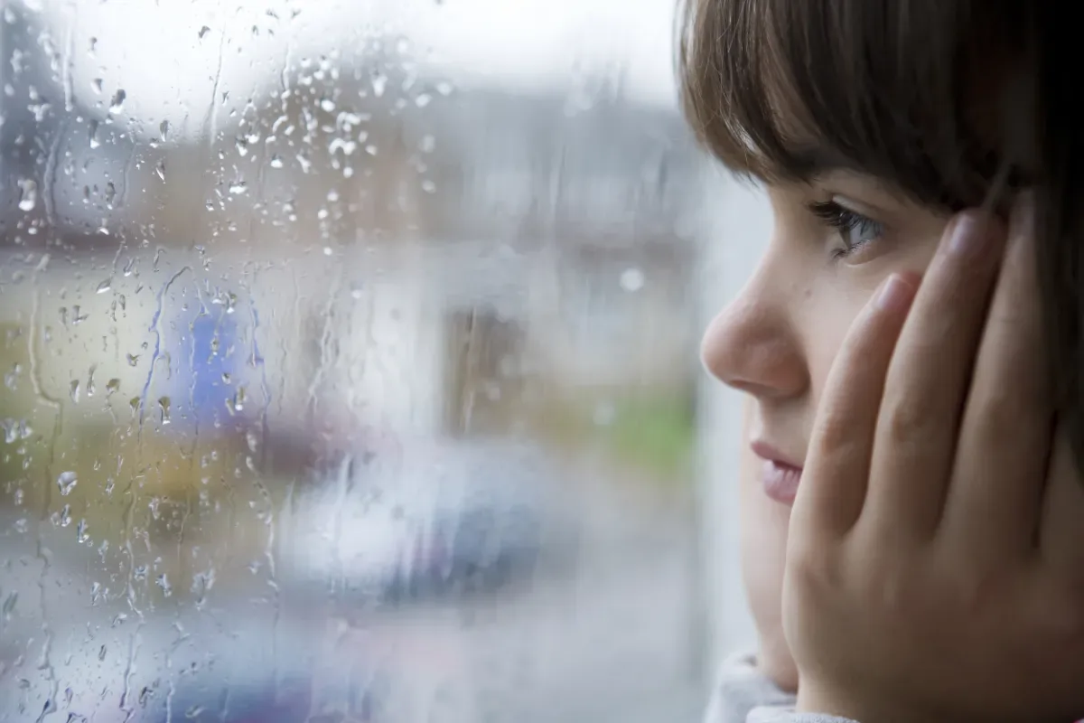 Onzekerheid bij kinderen: hoe help je je kind groeien? - kind kijkt bedroefd uit raam met regendruppels