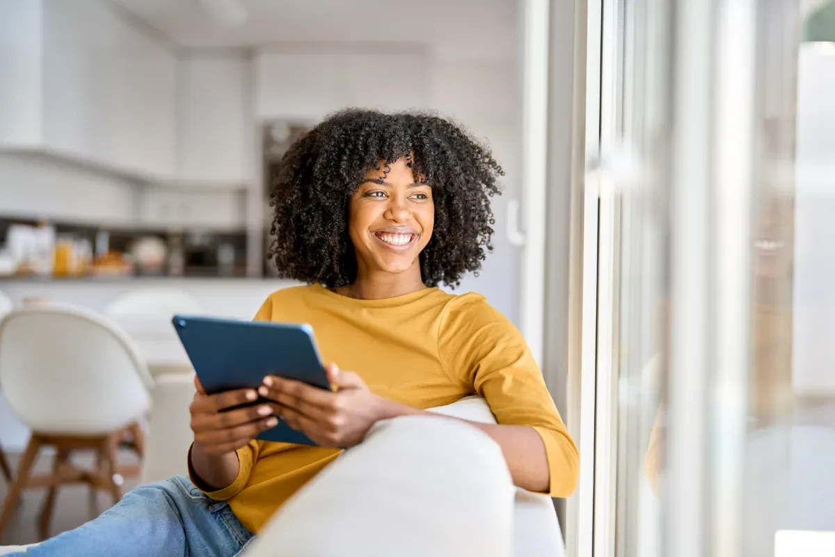 Positieve emotie - vrouw met tablet leunt vrolijk over bankstelleuning