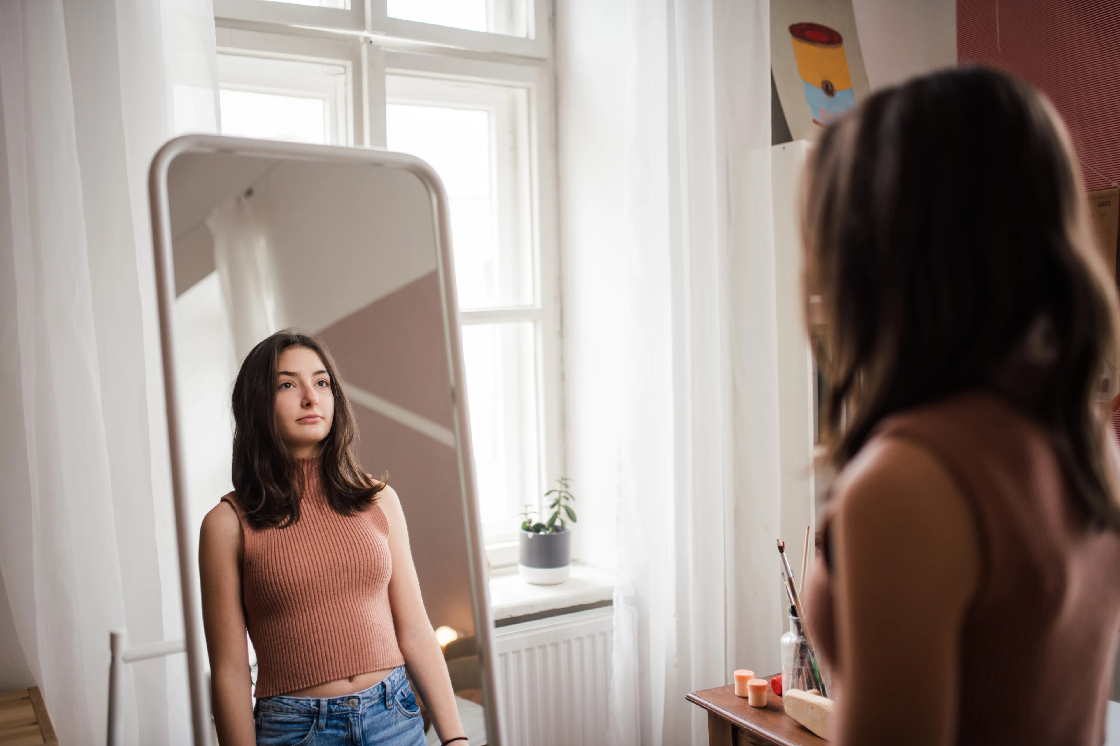 Hoe ontstaat een negatief zelfbeeld? - Jonge vrouw kijkt naar eigen reflectie in spiegel
