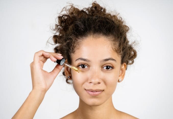 Young woman applying eye serum with a serum dropper.