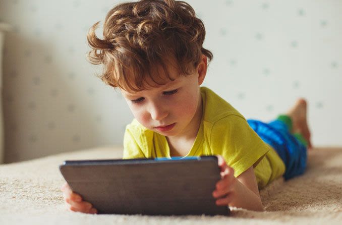 A child staring at a tablet screen while in bed.